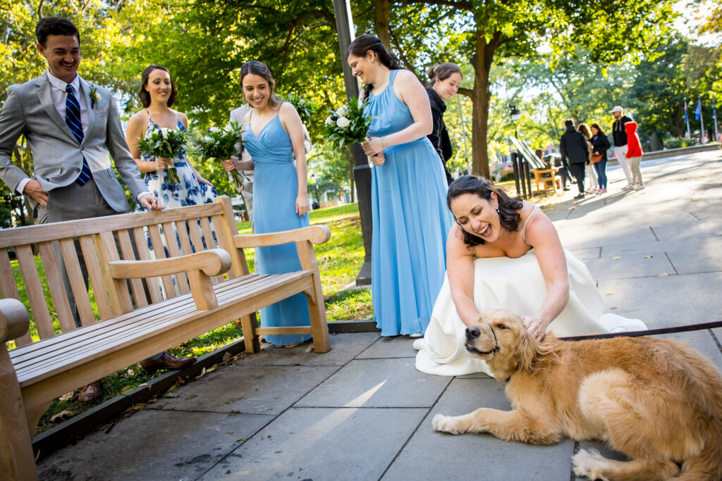 A woman in a wedding dress pets a dog in Rittenhouse Square Philadelphia